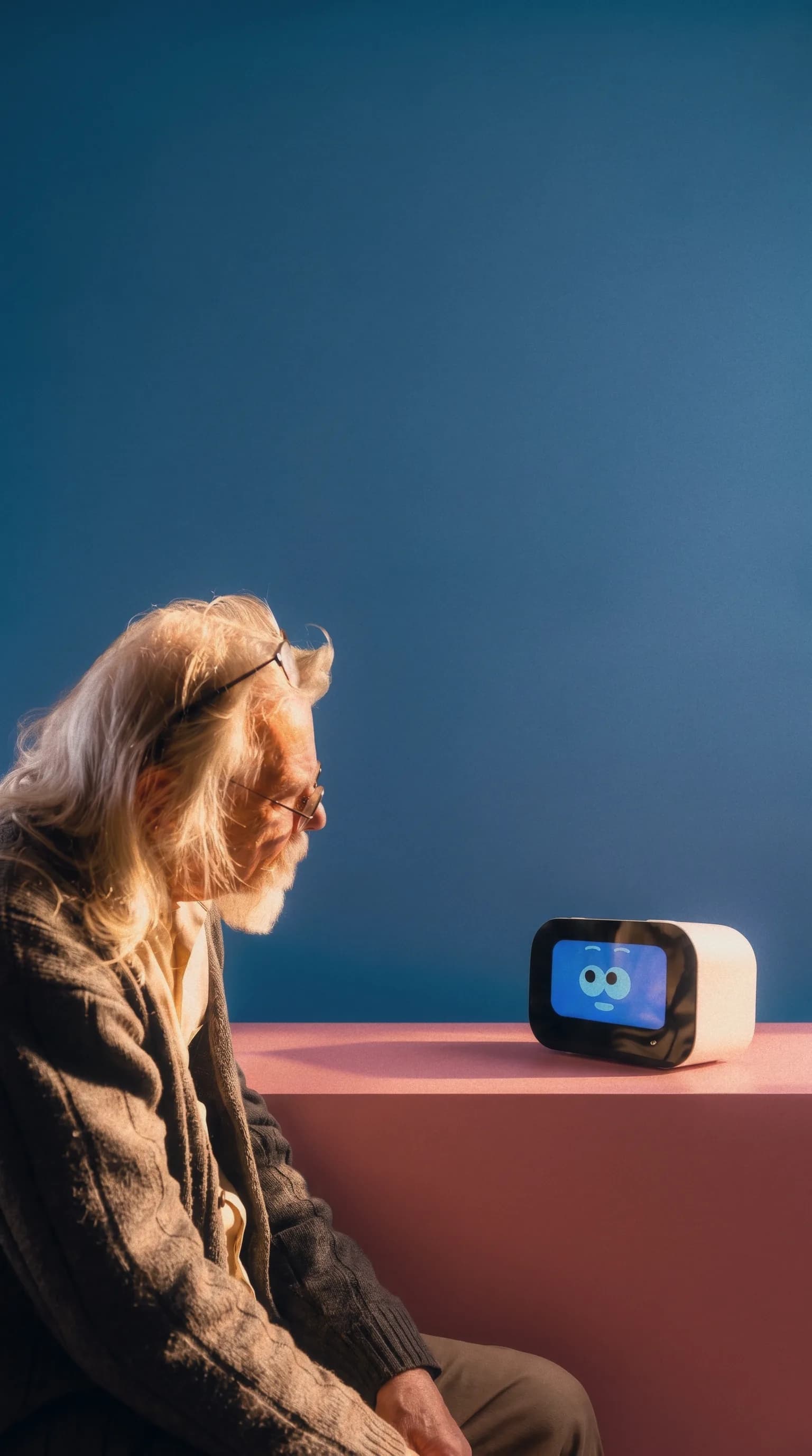 Older man with silver hair leaning in to meet Rhem, sitting on a pink table against a deep blue backdrop